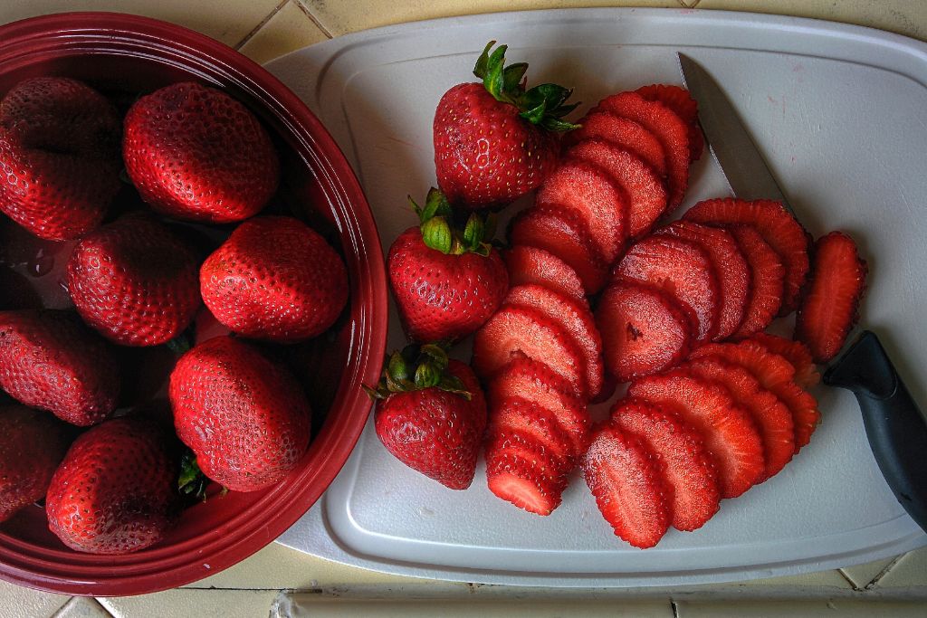 sliced strawberries on a chopping board alongside fresh ones on a bowl